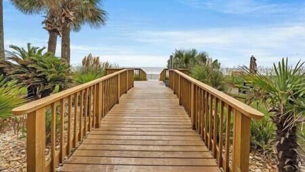 Une promenade en bois menant à la plage, bordée de palmiers et de végétation.
