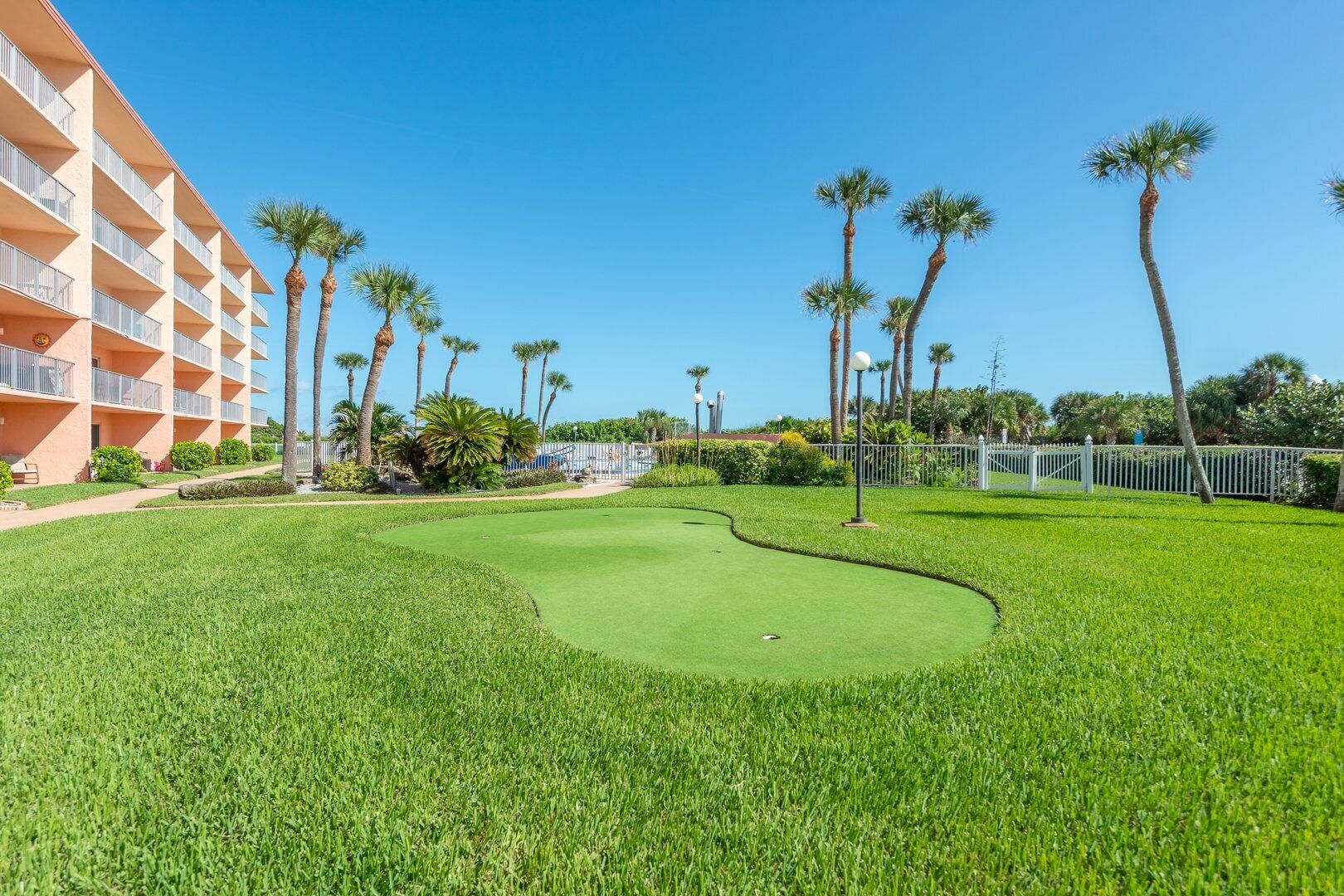 A golf course with a well-maintained green, palm trees, and a building with balconies.