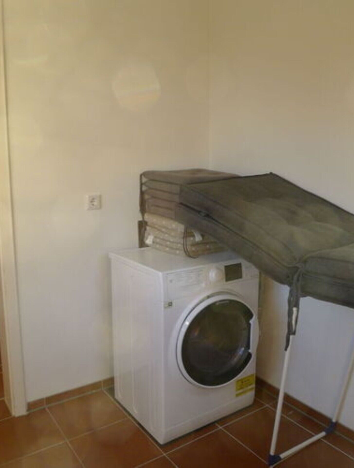 Eine kompakte, weiße Waschmaschine steht in einer Ecke eines Raumes mit Fliesenboden.
