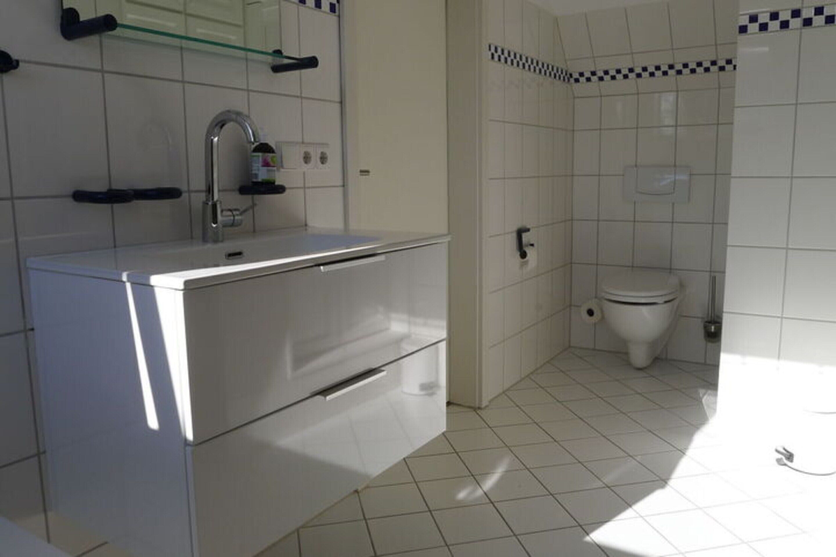 Et badeværelse med hvid vask, spejl og toilet.