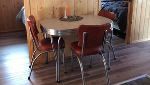 A wooden interior with a round table and four chairs, a bed with a cat, and a stone floor. - Cozy Cabin in Grand Beach.  (Grand Marais)