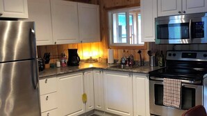 A kitchen with white cabinets, a stainless steel refrigerator, a microwave, and an oven. - Cozy Cabin in Grand Beach.  (Grand Marais)