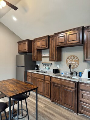 A modern kitchen with wooden cabinets, a granite countertop, a stainless steel refrigerator, and a bar stool.