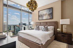 Ein modernes Hotelzimmer mit einem großen Bett, Blick auf die Stadt, einem Chandelier und einem Gemälde an der Wand.