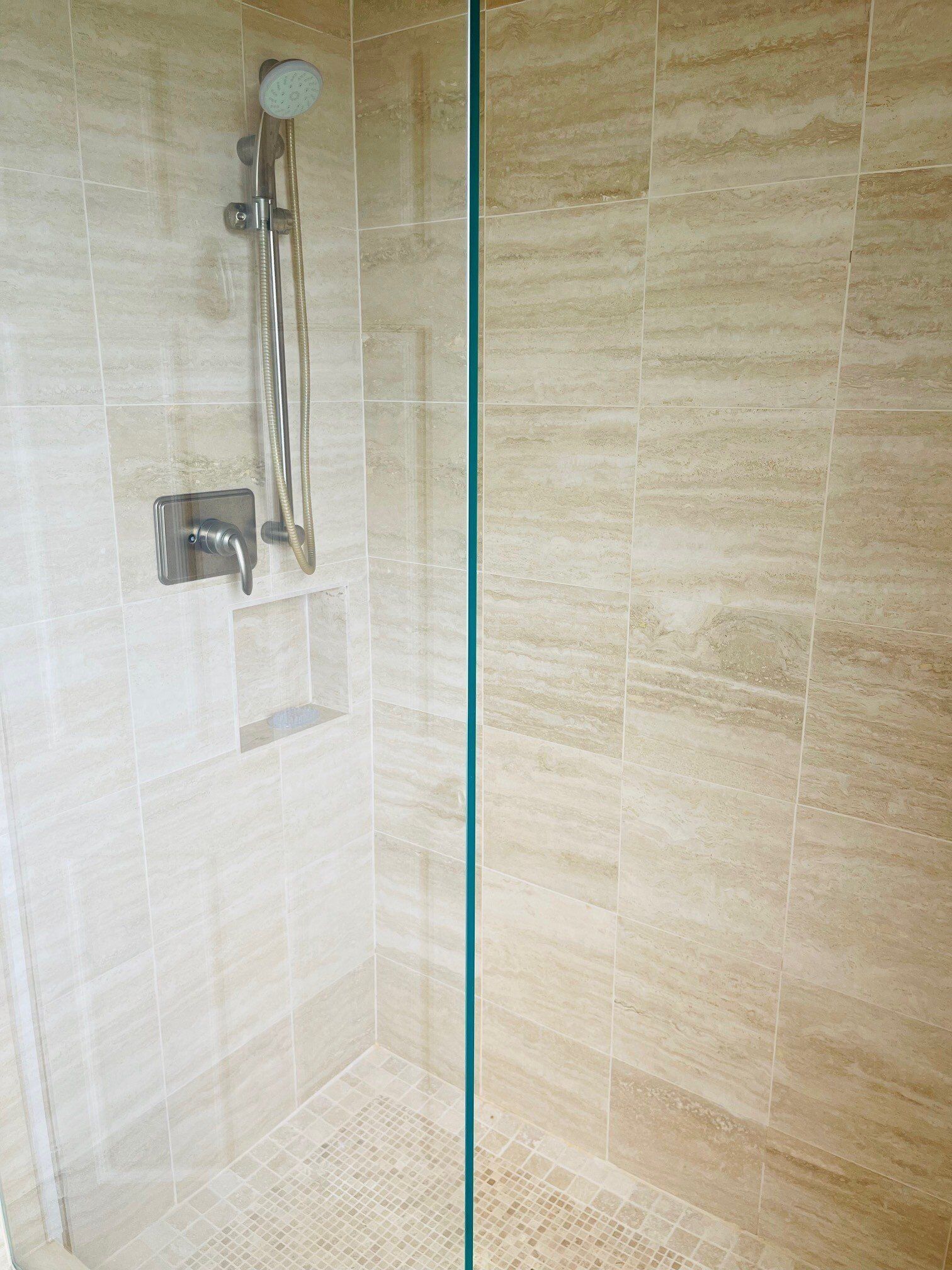 Un espace douche doté d’une paroi en verre, d’un pommeau de douche à main et d’un panneau de commande fixé au mur.
