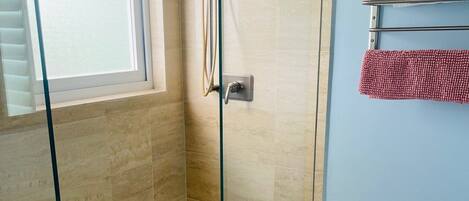 A bathroom with a glass-enclosed shower, a toilet, and a window.