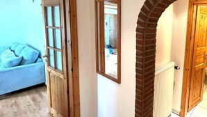 Un pasillo con una puerta de madera, un espejo y un arco de ladrillo que da a otra habitación.