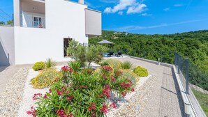 Un bâtiment moderne de couleur blanche, doté d’un balcon, entouré d’un jardin de gravier agrémenté de diverses plantes et fleurs.