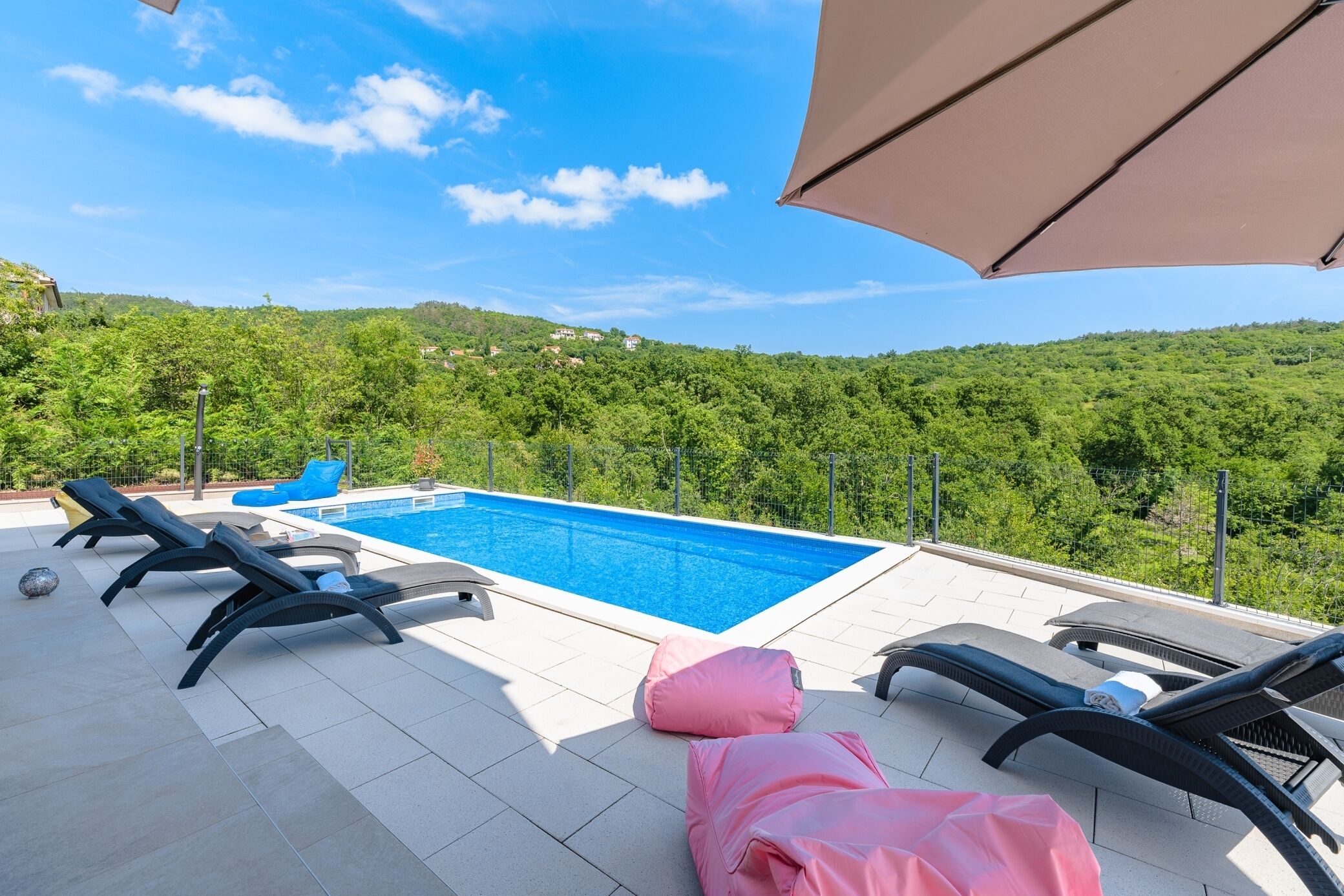 A rooftop pool area with lounge chairs and a view of a forested hillside.