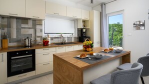 Une cuisine moderne dotée d’un îlot central, d’un four encastré et d’un coin petit-déjeuner avec des croissants et des fruits.