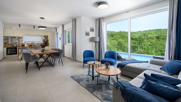 Un salon moderne comprenant un canapé, deux fauteuils bleus, une table basse et un coin repas avec une table et des chaises.