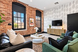 Een moderne woonkamer met bakstenen muren, grote ramen, een flatscreen-tv en een groene bank.