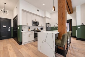 A modern kitchen with white cabinets, a central island, stainless steel appliances, and a wooden accent wall.