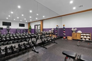 Et fitnessrum med vægttræningsudstyr, et spejl og et fjernsyn på væggen.