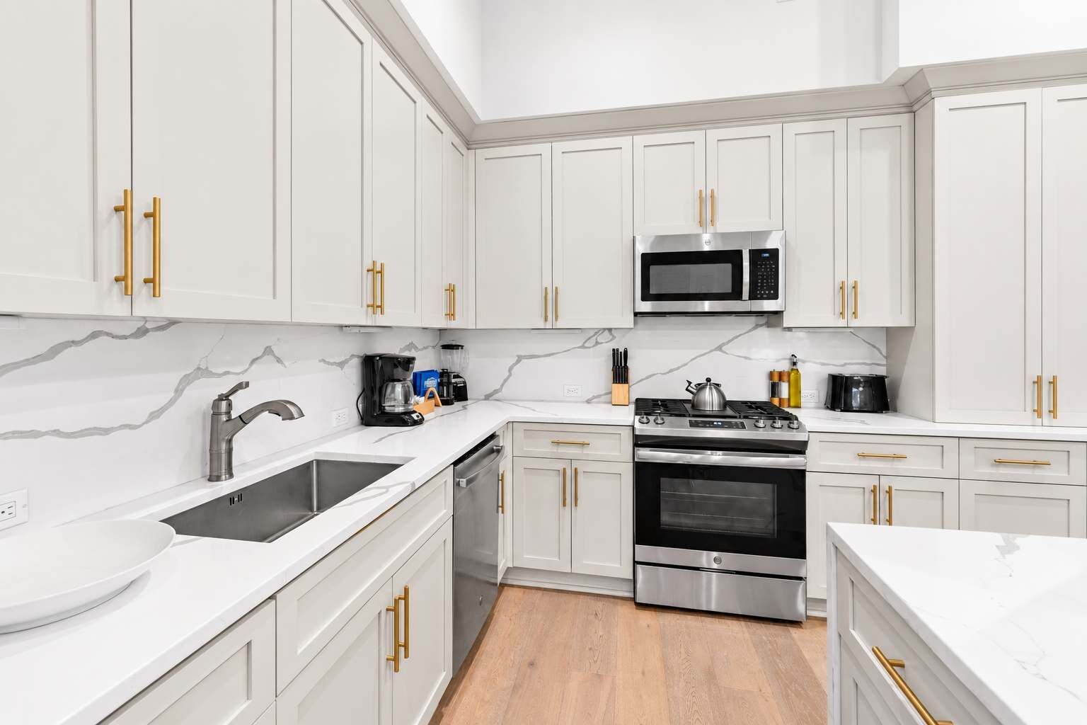 A modern kitchen with white cabinets, stainless steel appliances, and marble countertops.