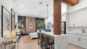 A modern kitchen with white cabinets, a marble island, and a dining area with a sofa and chairs. - LUXE Suite 2BR 2BA Steps from Superdome Hotel (New Orleans)
