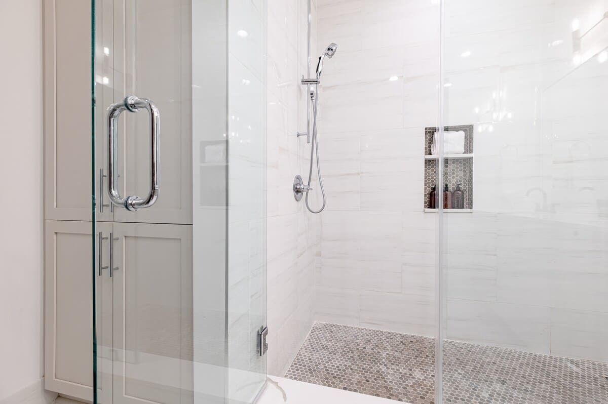 Een moderne badkamer met een douchecabine van glas, een douchegedeelte betegeld met witte tegels en een glazen kastje.