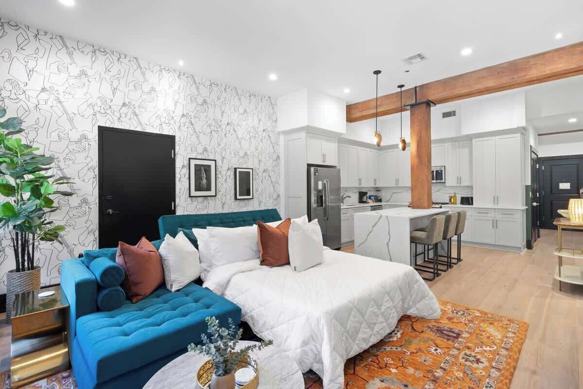 Une chambre moderne avec un grand lit, un canapé bleu et une cuisine en arrière-plan.