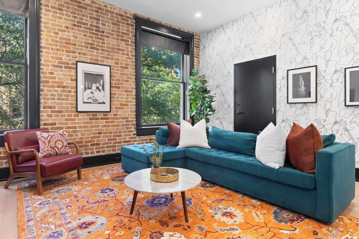 A room with a brick wall, a blue sofa, a red armchair, and a patterned rug.
