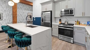 A modern kitchen with a central island, stainless steel appliances, and teal bar stools. - Prime Downtown Suite Location Heated Pool Gym Hotel (New Orleans)