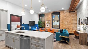 A modern kitchen with a central island, a dining area with a brick wall, and a living space with a blue sofa. - Prime Downtown Suite Location Heated Pool Gym Hotel (New Orleans)
