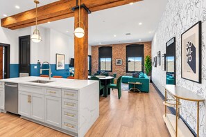 A modern kitchen with a marble island, wooden beams, and a dining area with a green sofa and table. - Spa Bath Rooftop Pool BBQ Gameroom Hotel Suite (New Orleans)