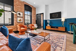 A modern living room with brick walls, a sofa, armchairs, a coffee table, and a TV.