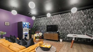 A modern living room with a sofa, a coffee table, a TV, a vending machine, and a patterned wall. - Modern Comfort Suite Pool Gym Luggage Lockers Hotel (New Orleans)