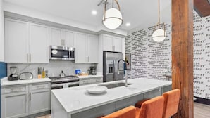 A modern kitchen with white cabinets, stainless steel appliances, and a central island with orange chairs.