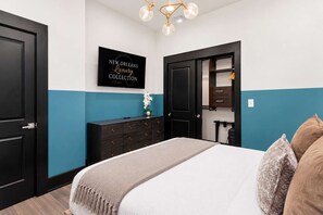 A bedroom with a bed, dresser, and a wall-mounted TV displaying 'NEW ORLEANS Luxury Collection'.