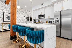 A modern kitchen with a marble island, stainless steel appliances, and teal bar stools. - Game Room  Gym  Pool  Rooftop  Downtown Suite Hotel (New Orleans)