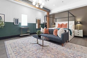 A modern bedroom with a four-poster bed, a sofa, a coffee table, and a bedside table with lamps.