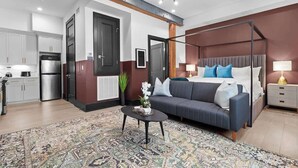 Camera d'albergo moderna con un letto a baldacchino, un divano, un tavolino da caffè, un angolo cottura e un tappeto grande con motivo decorativo.