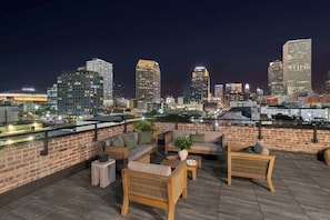 Une terrasse sur le toit, aménagée avec du mobilier d’extérieur, un mur en briques et une vue sur les toits de la ville la nuit.