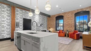 A modern kitchen with a marble island, a brick accent wall, and a large window.