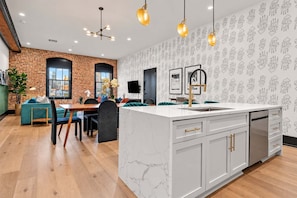 A modern kitchen with a marble island, white cabinetry, and pendant lighting.