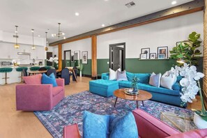 A modern hotel lobby with a kitchen area, a seating area with sofas and chairs, and a large window with a view.