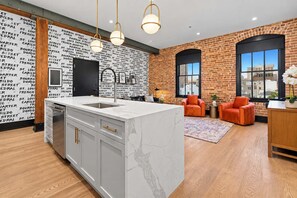 A modern kitchen with a marble island, a brick wall with text, and a large window. - HUGE 4BD 4BA with 2 Queen Sleeper Sofas! Hotel Suite (New Orleans)