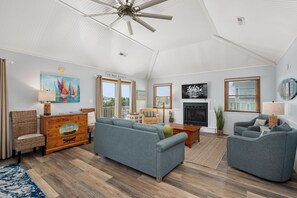 A spacious living room with a high ceiling, a fireplace, a television, and a large window.