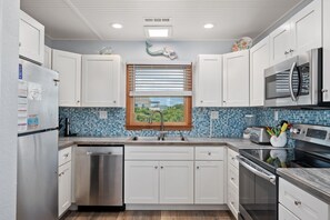 A modern kitchen with white cabinets, a stainless steel refrigerator, a microwave, and a dishwasher. - Second Wind: Oceanside with Views, Close to Beach and Lighthouse! (Corolla)