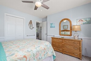 A bedroom with a bed, dresser, ceiling fan, and wall art.