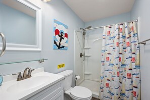 Un baño con un lavabo blanco, un espejo, un inodoro y una cortina de ducha con motivos náuticos.