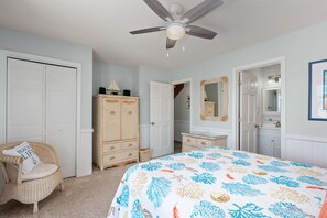 Un dormitorio con cama, ventilador de techo, armario, cómoda, silla y espejo.