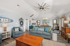 A spacious living room with a high ceiling fan, a wooden coffee table, and a gray sofa with colorful cushions.