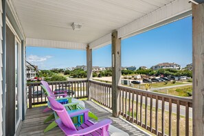 A covered porch with colorful Adirondack chairs, a view of a parking lot, and houses in the background.