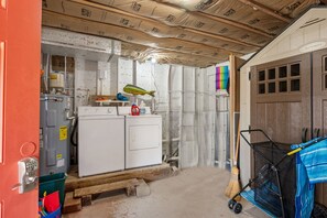A utility room with a water heater, washing machine, and a broom. - Second Wind: Oceanside with Views, Close to Beach and Lighthouse! (Corolla)