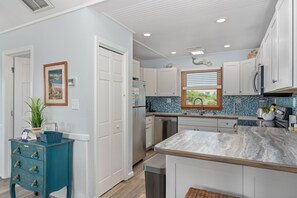 A modern kitchen with white cabinets, a marble countertop, and a view of the outdoors. - Second Wind: Oceanside with Views, Close to Beach and Lighthouse! (Corolla)