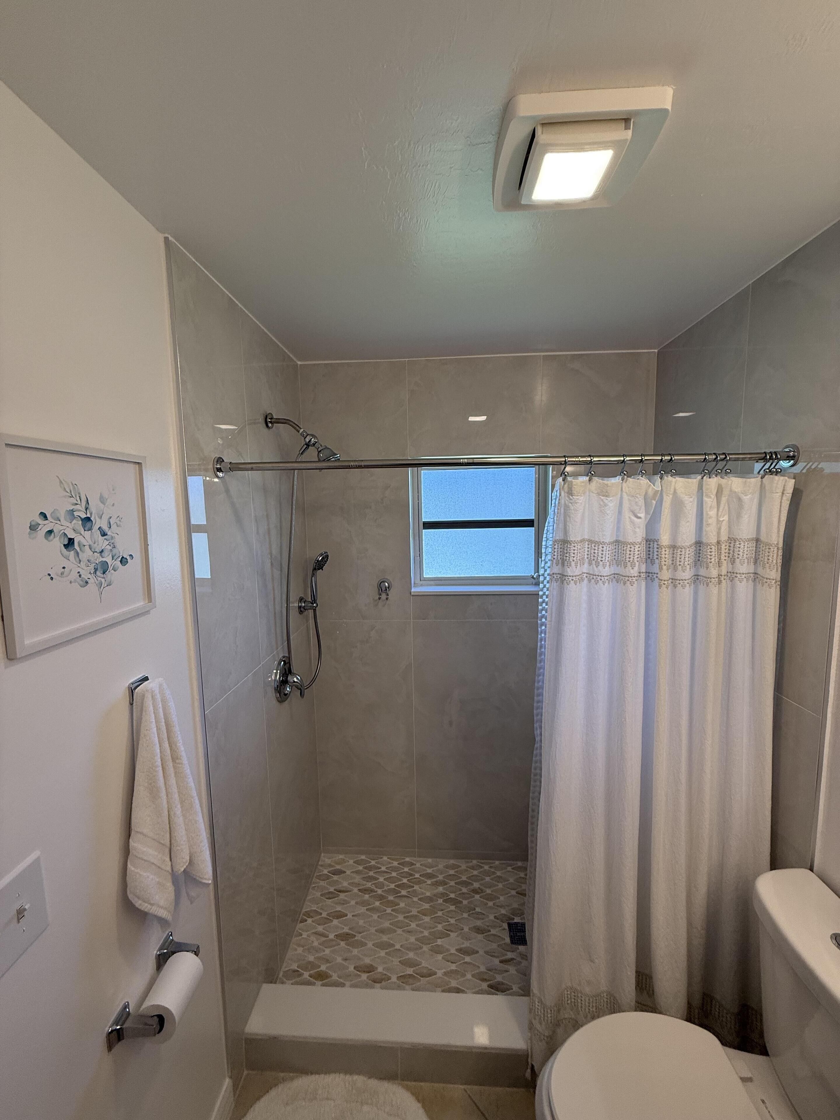 Un baño moderno con ducha de vidrio, inodoro y una ventana pequeña.