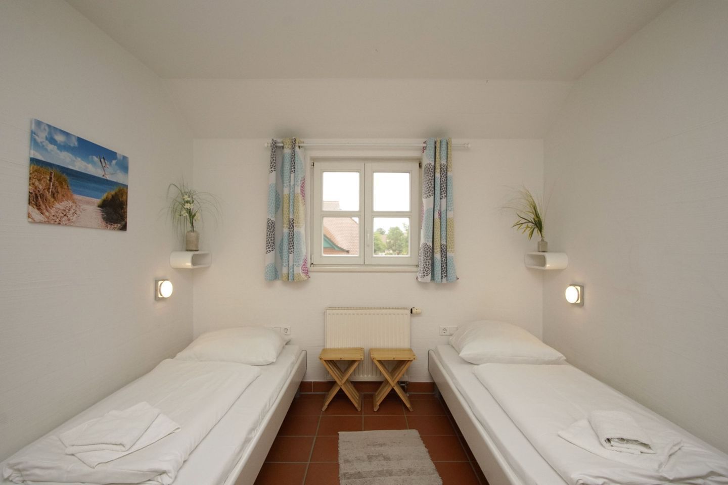 A twin room with two single beds, a window with curtains, a radiator, and a small plant on a shelf.