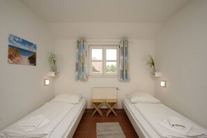 A twin room with two single beds, a window with curtains, a radiator, and a small plant on a shelf.